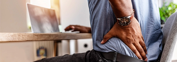A person sitting on a chair while holding their lower back.