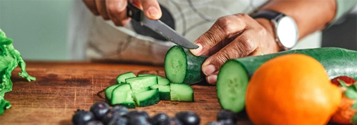 Acupuncture Flower Mound TX Man Cutting Food A person cutting a cucumber on a wooden cutting board.